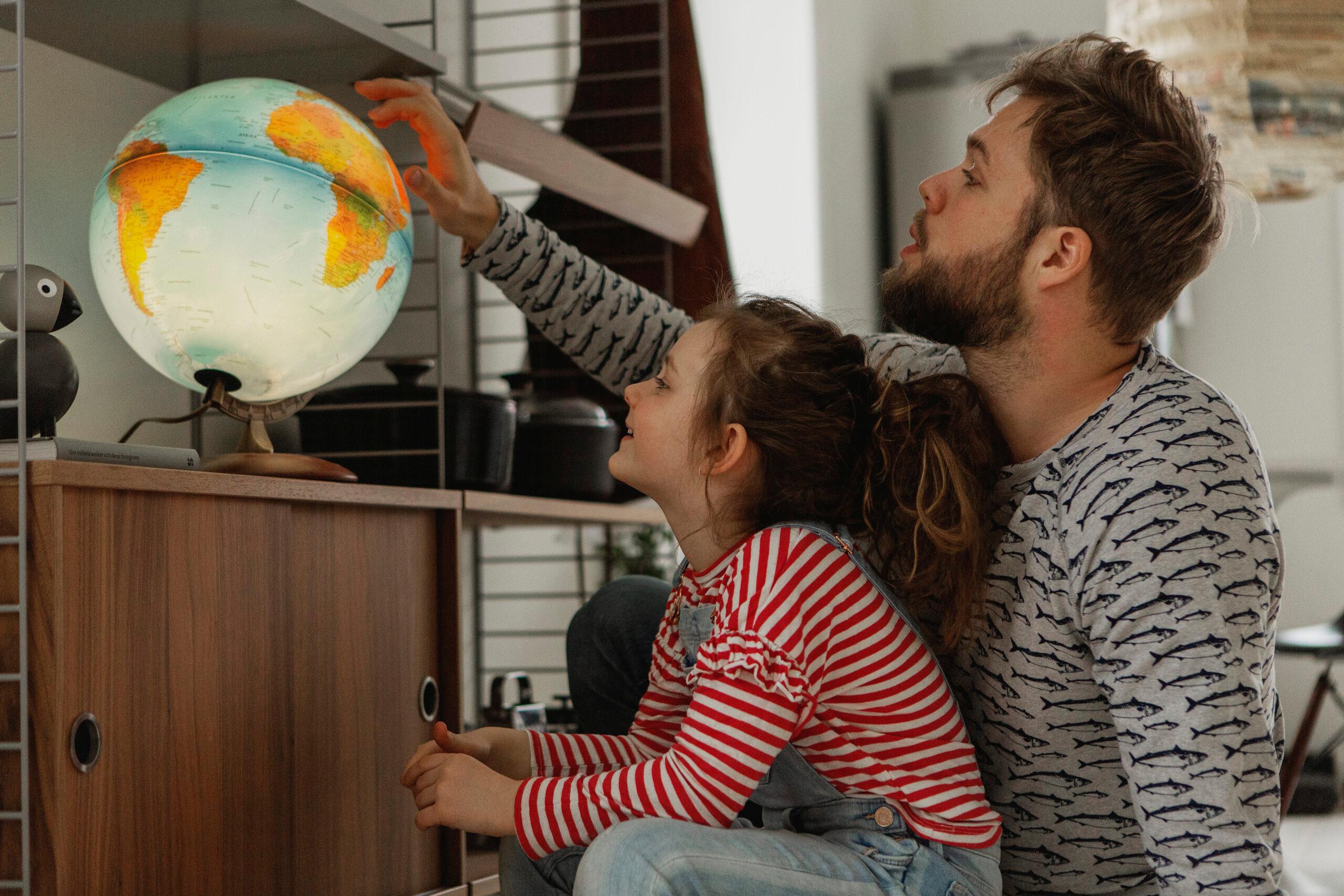 A child and her father looking at a globe lamp.