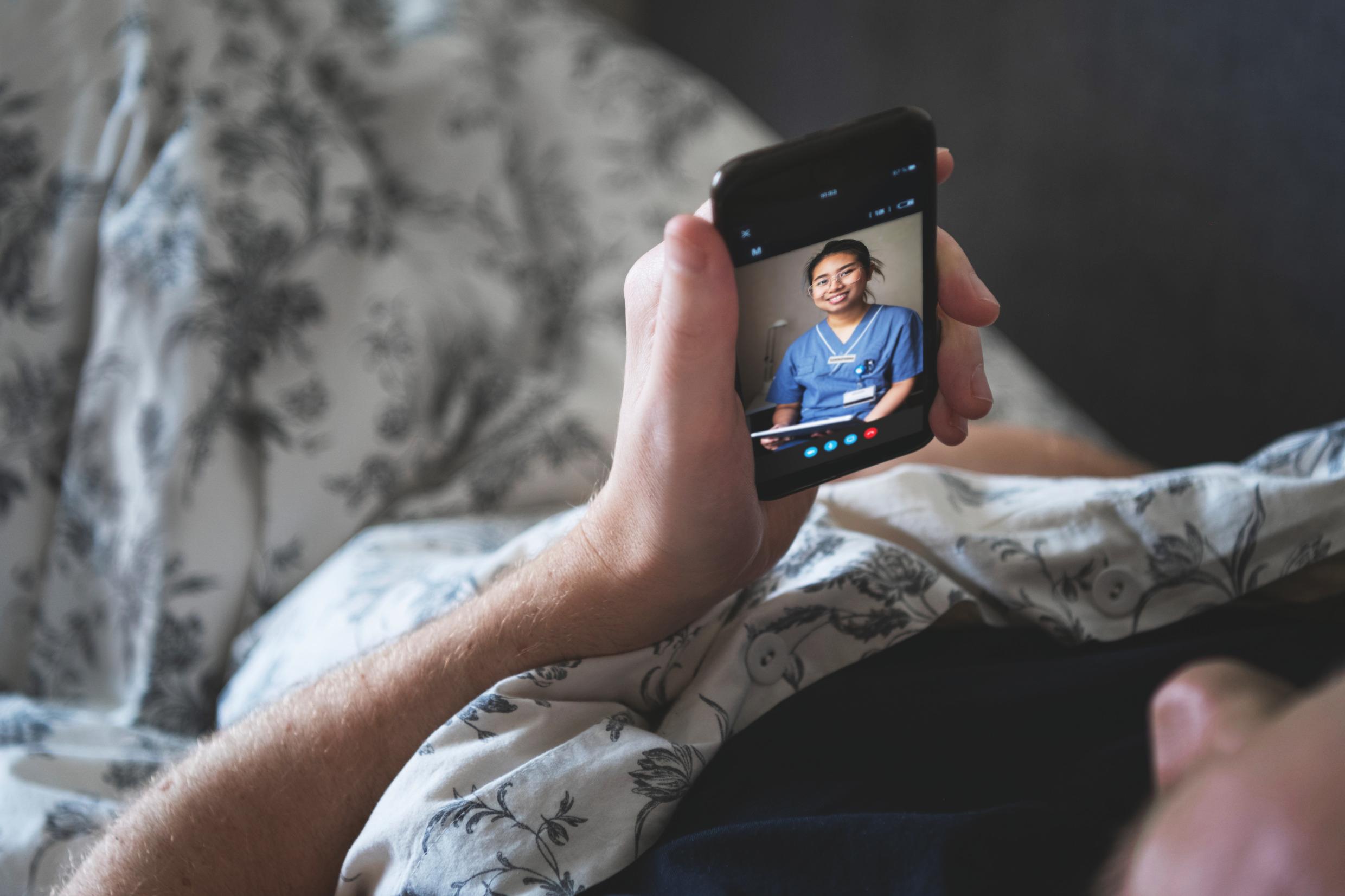 A person in bed is in an online conversation over the phone with a healthcare professional.