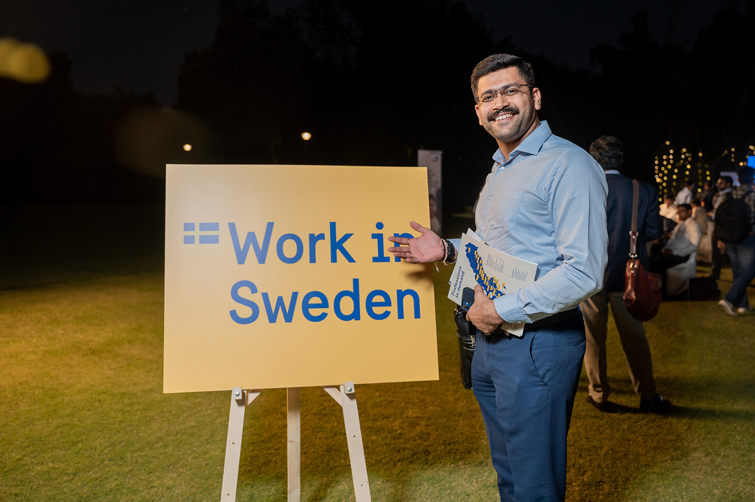 A happy man standing in front of the Work in Sweden-sign