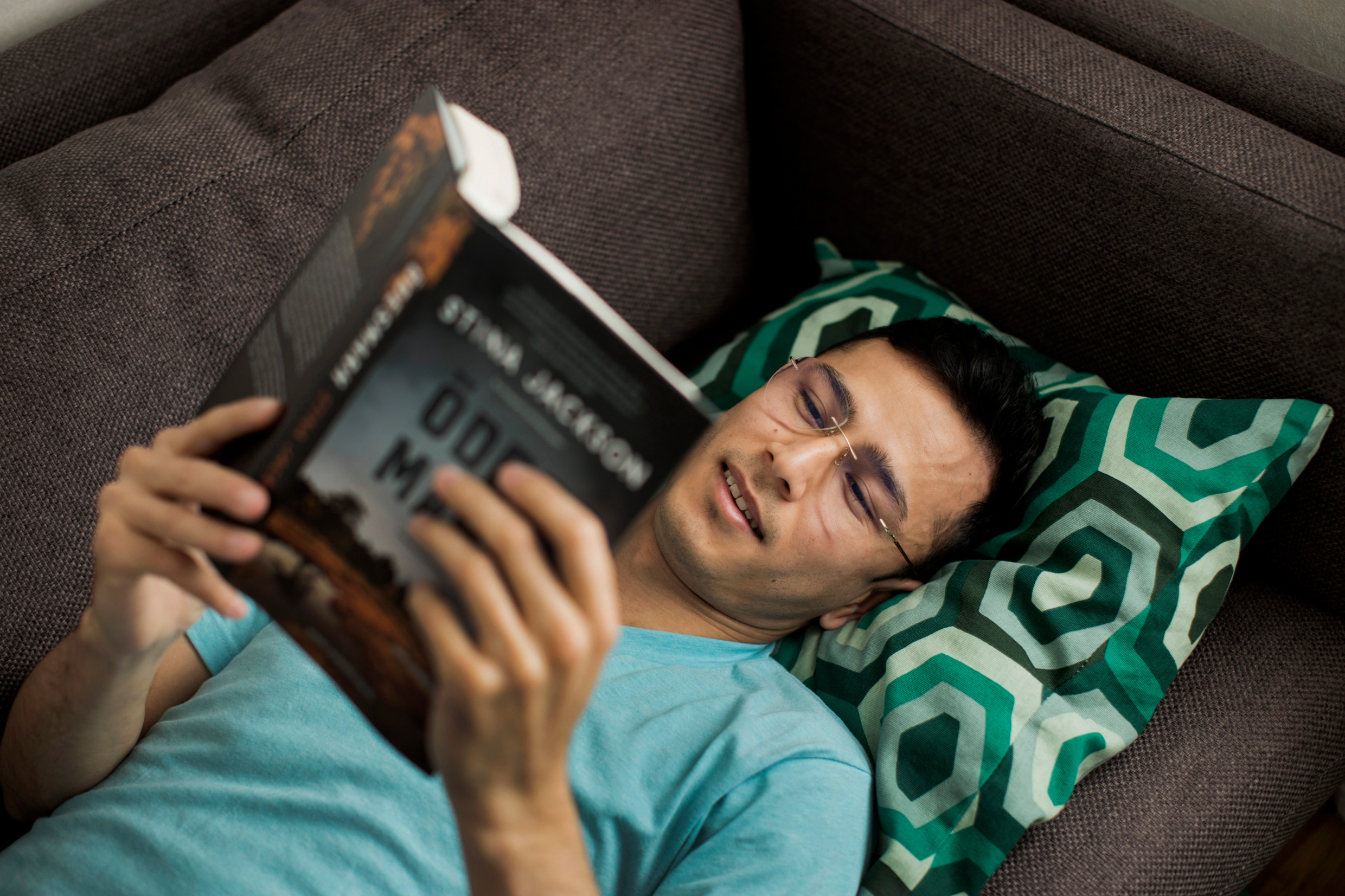 A man lies in a sofa, holding a book.