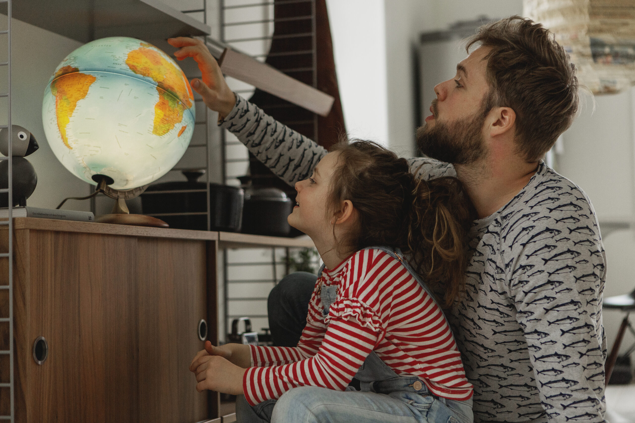 A child and her father looking at a globe lamp.