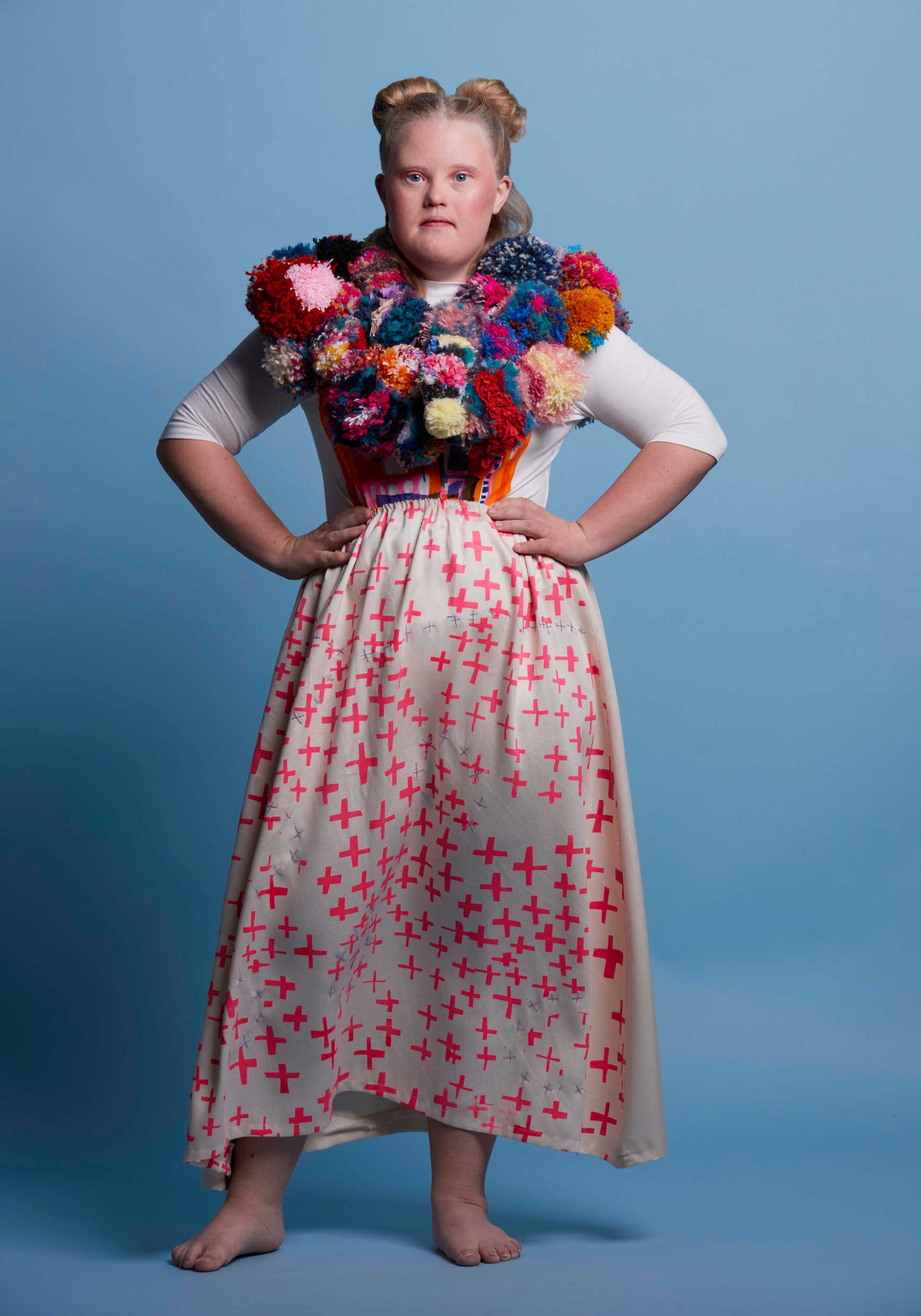 A girl with Downs syndrom in a skirt and with a large pom-pom collar around her neck.